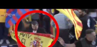 Un hombre sube al escenario de la marcha independentista con una bandera de España y el lema ‘Viva el Rey’