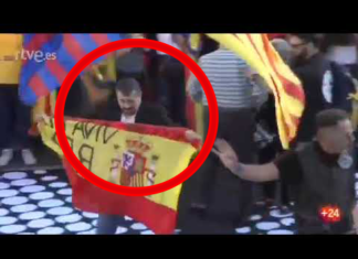 Un hombre sube al escenario de la marcha independentista con una bandera de España y el lema ‘Viva el Rey’