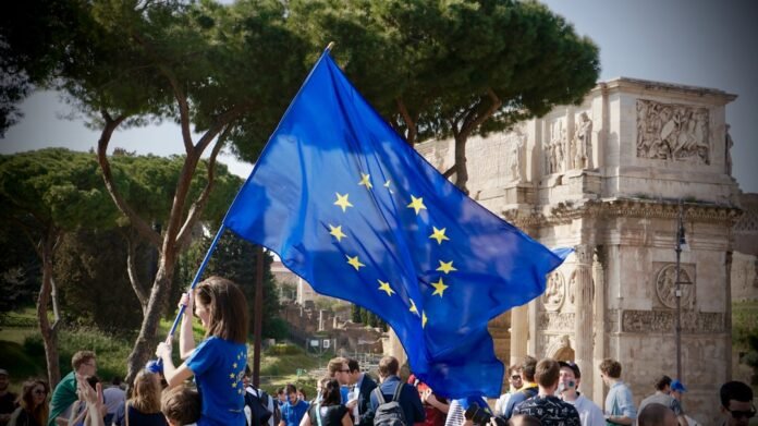 image_1775901625437 a young girl holding a european flag in front of a crowd of people