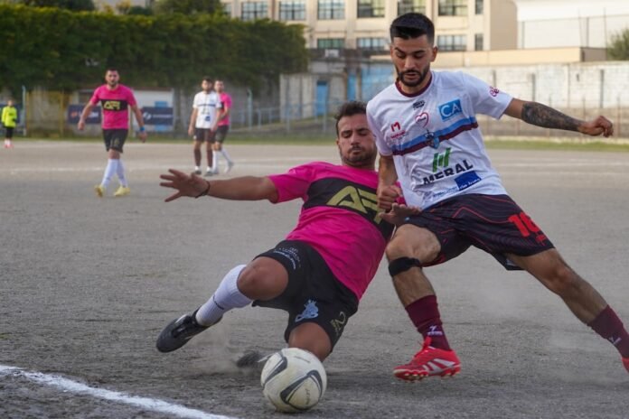 Two men playing soccer on a dirt field.