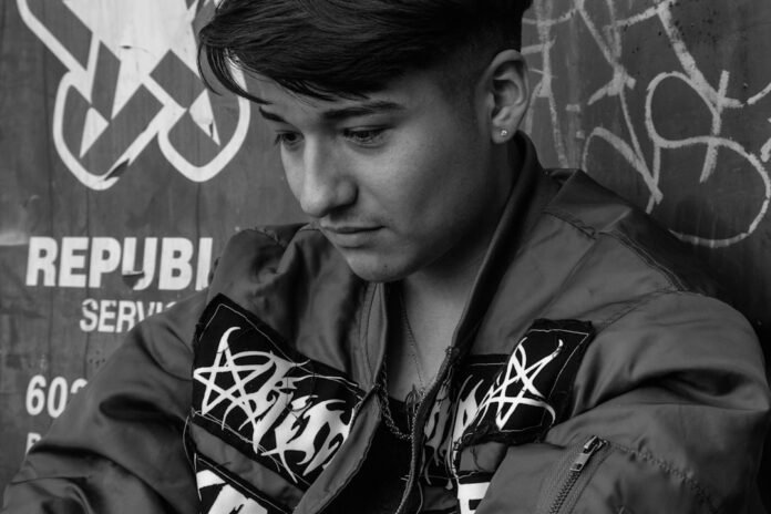 a young man in a leather jacket leaning against a wall