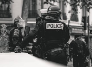 Controversia por agresión policial a manifestante en Valencia: cuando la fuerza pública traspasa los límites grayscale photo of Police standing and leaning on wall