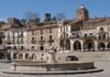 Extremadura experimenta un adelanto del calor veraniego con temperaturas cercanas a los 40 grados Old buildings surround a fountain in a sunny plaza.