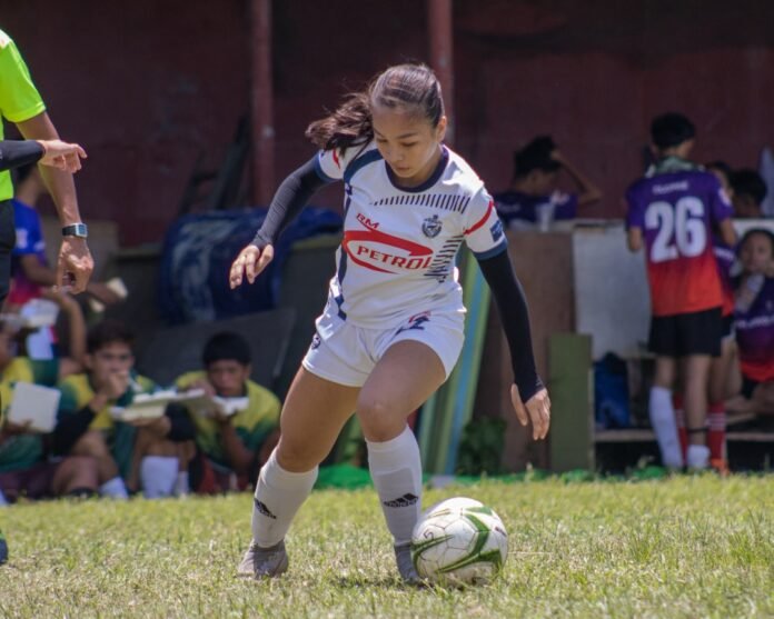 a young girl kicking a soccer ball on a field
