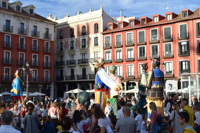 a group of people in clothing performing in front of a crowd with Plaza Mayor, Madrid in the background