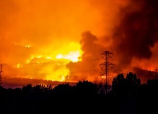 Incendios Simultáneos en Cataluña: El Gran Desafío Logístico que Pone a Prueba los Límites de la Protección Civil A massive wildfire rages under an orange, smoke-filled sky.