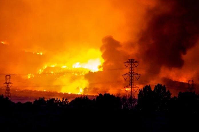 A massive wildfire rages under an orange, smoke-filled sky.
