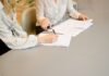 El Nuevo Contrato Laboral: Cuando el Valor Profesional Va Más Allá de las Herramientas que Dominas woman signing on white printer paper beside woman about to touch the documents