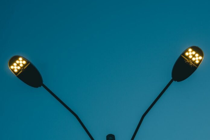 Two modern led streetlights illuminate against a blue sky