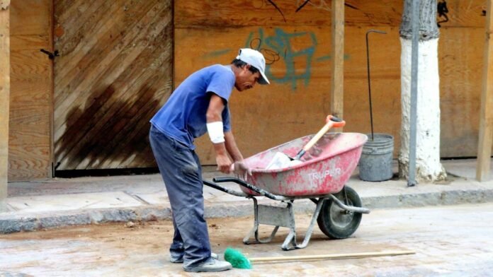 man in blue polo shirt and blue denim jeans holding red wheelbarrow