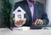 El coste de demonizar la propiedad: cómo una generación perdió la oportunidad de comprar vivienda man holding model house at desk with calculator
