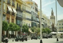 DANA sobre España: Qué es, cómo funciona y qué zonas se verán más afectadas por las lluvias y tormentas Seville street with historic buildings, parked scooters, and giralda tower