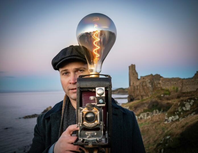 a man holding a camera with a light bulb on top of it
