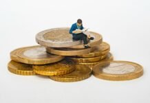 Cuentas Remuneradas Sin Comisiones: Cómo Sacar el Máximo Partido a Tus Ahorros en el Entorno Actual Miniature person sitting on stack of coins reading newspaper