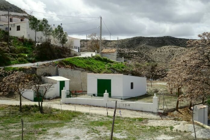 White buildings with green doors in a rural landscape under a cloudy sky