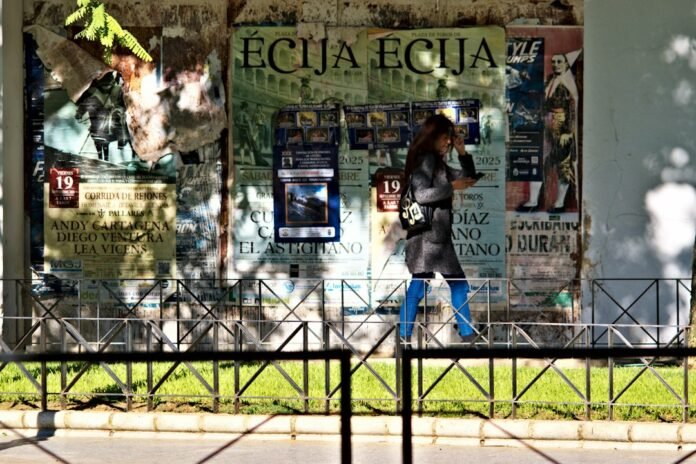 Woman walks past a wall of torn posters