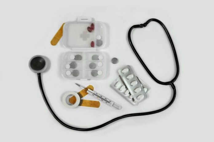 image_1793455235575 A stethoscope, pill organizer, blister packs, thermometer, and adhesive bandages on white